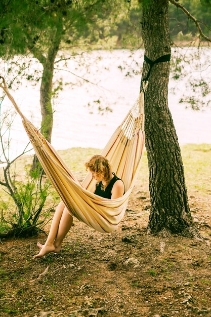 Woman sitting in hammock on riverbank