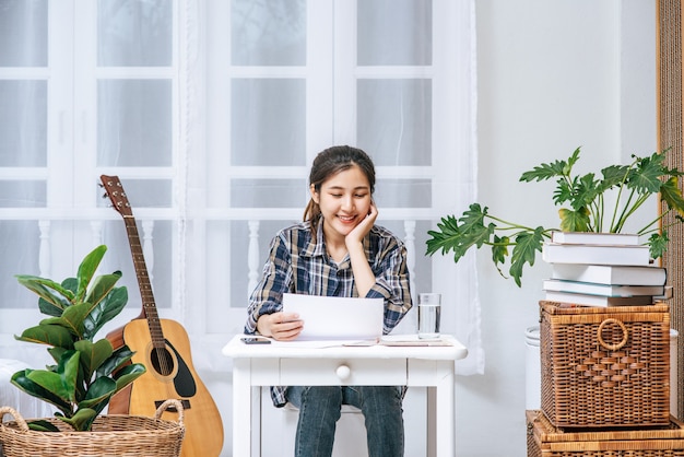 机に喜んで座っている女性が書類を分析します。