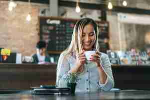 Free photo woman sitting happily drinking coffee in cafe