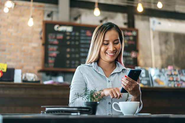 コーヒーショップでスマートフォンを喜んで働いて座っている女性