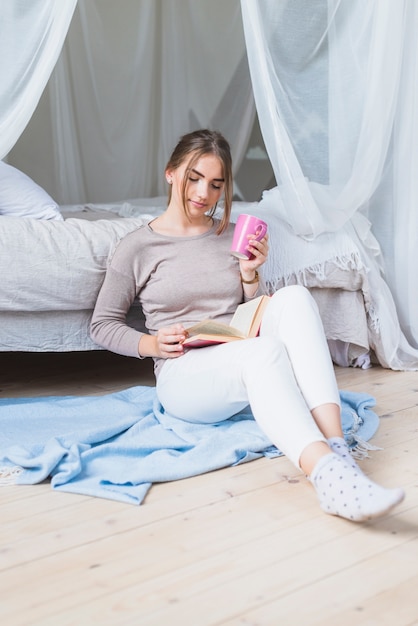 Woman sitting on hardwood floor reading book in bedroom