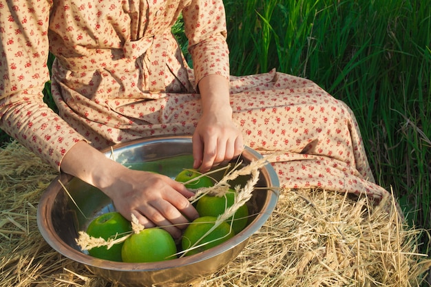 緑の牧草地にリンゴと干し草の山に座っている女性