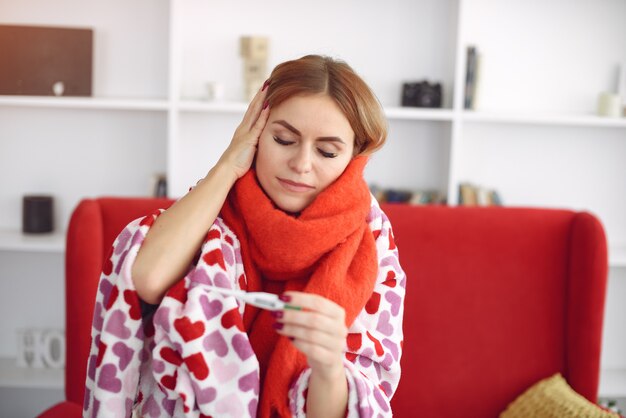 Женщина сидит дома с простудой и измеряет температуру