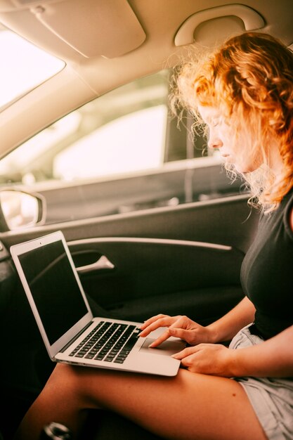 Woman sitting inside car and using laptop