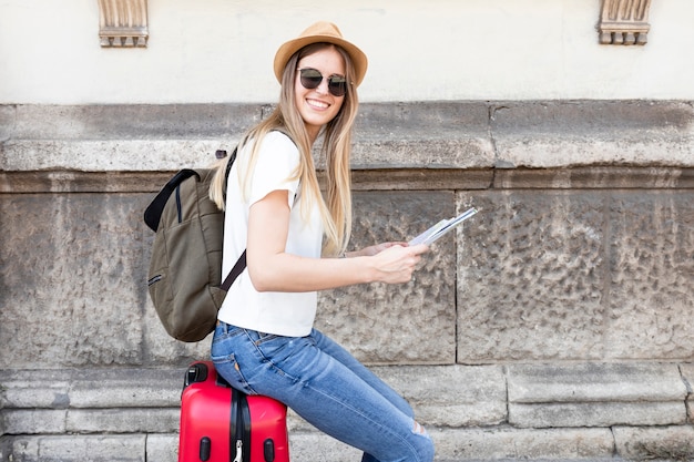 Woman sitting on luggage smiles at camera