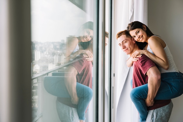 Woman sitting on man back near window 