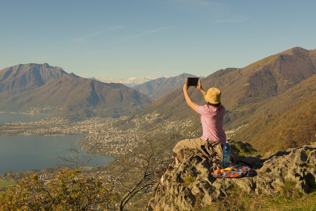山に座って、スイスの美しい湖の景色の写真を撮る女性
