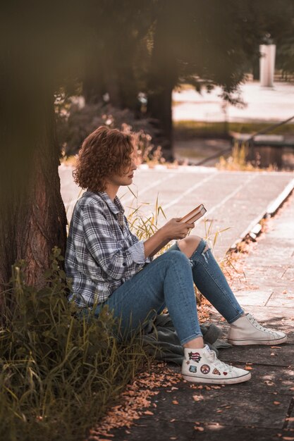 Woman sitting near tree and holding books 