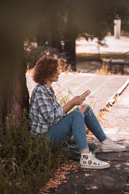 Женщина, сидящая возле дерева и проведение книг