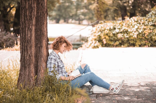 木の近くに座って読書をする女性