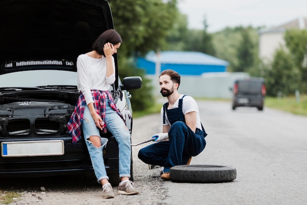 Бесплатное фото Женщина, сидящая на машине и мужчина, меняющая шину