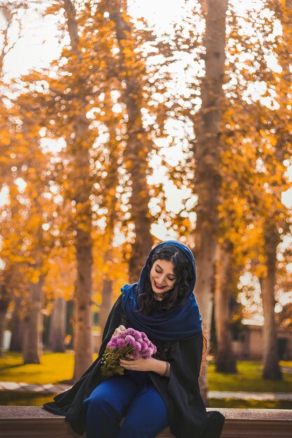 Женщина сидит в парке и держит букет цветов