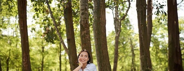 晴れた日の日陰で木に寄りかかってお気に入りの本を読んで公園に座っている女性