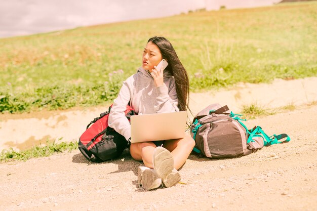 Free Photo woman sitting on road and talking on mobile phone among backpacks