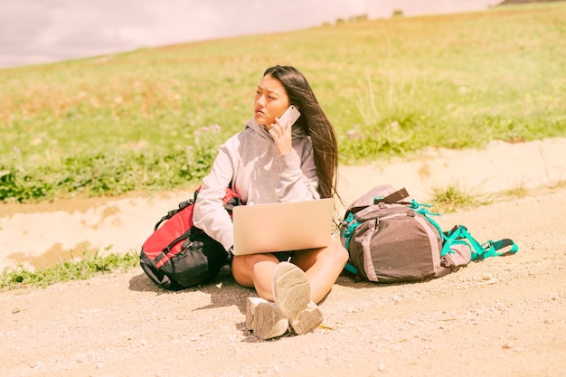 Woman sitting on road and talking on mobile phone among backpacks