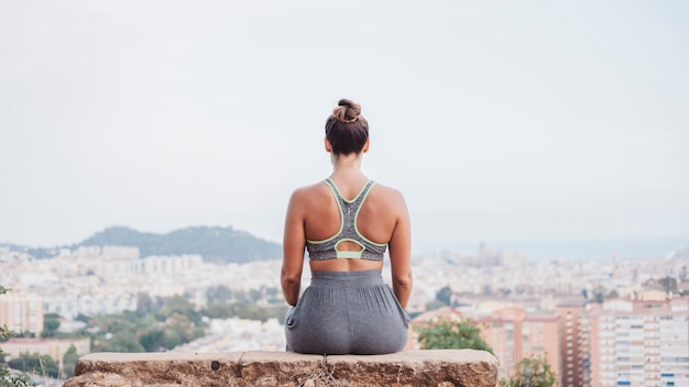 Woman sitting on rock in front of city