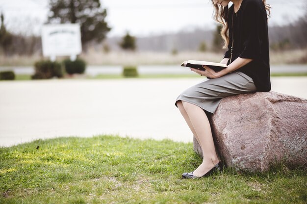 Woman sitting on a rock while reading a book