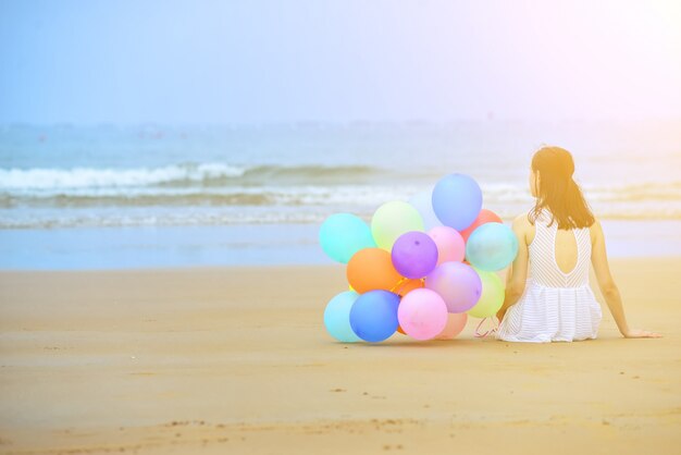 Woman sitting on the sand next to a bunch of balloons