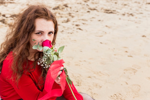 Free photo woman sitting on sea shore and sniffing rose