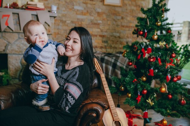 Woman sitting in a single armchair with her baby and a guitar next to it