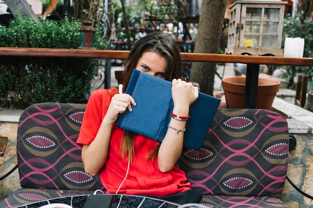 Free photo woman sitting on sofa hiding behind an open book