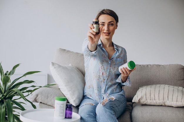 Woman sitting on sofa and holding pills vitamins