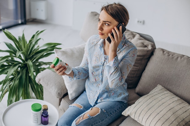 Woman sitting on sofa and holding pills vitamins