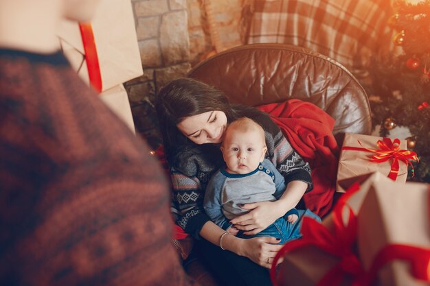 Woman sitting on a sofa with a baby in her arms and with a mountain of brown gifts with red bow