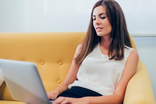 Free photo woman sitting on a sofa with a laptop on legs