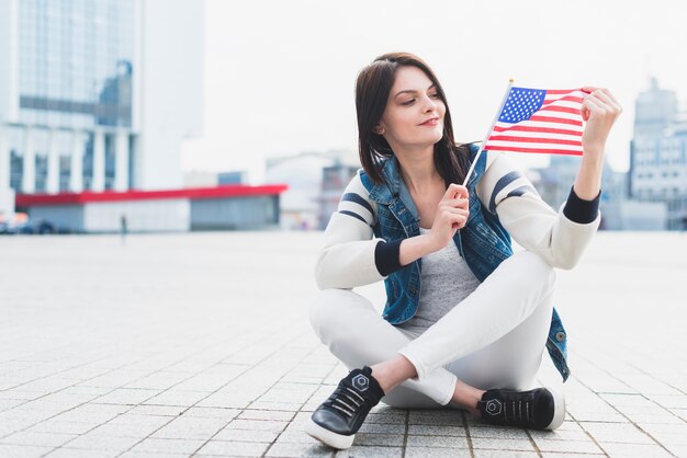 Женщина сидит на площади и держит в руке американский флаг