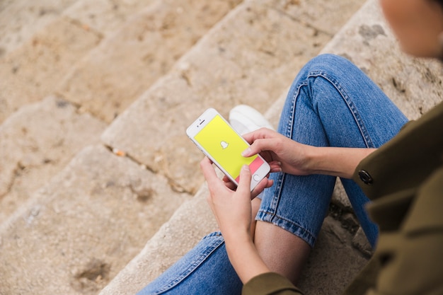 스마트 폰에 snapchat 앱을 사용하여 계단에 앉아있는 여자