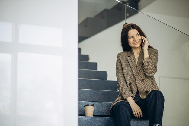 Woman sitting on stairs drinking coffee and using phone