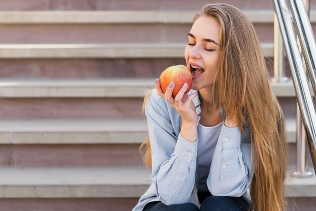 Женщина сидит на лестнице и ест яблоко
