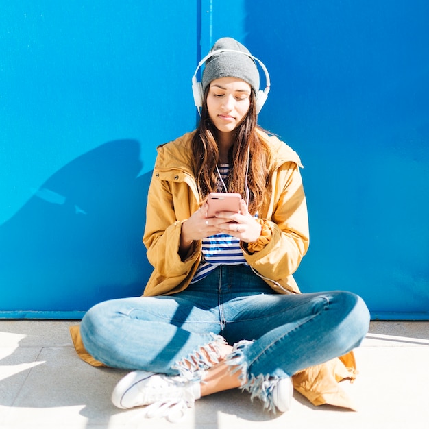 woman sitting in sunlight in front of door using cellphone wearing headphones