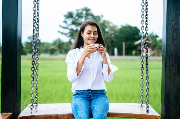 Free photo woman sitting on a swing and holding a cup of coffee