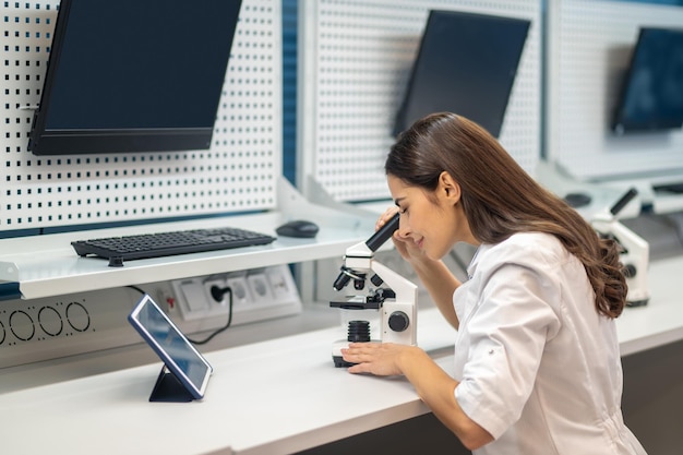 Женщина сидит за столом и смотрит в микроскоп