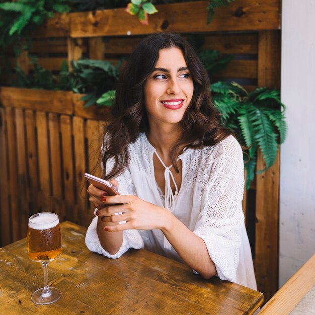 Woman sitting at table with beer and smartphone