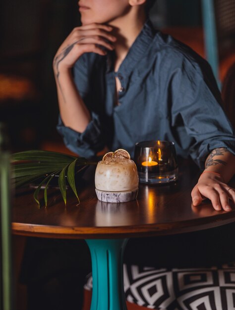 A woman sitting at the table with cocktail and burning candle side view