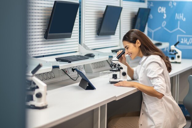 Женщина сидит за столом и работает с микроскопом