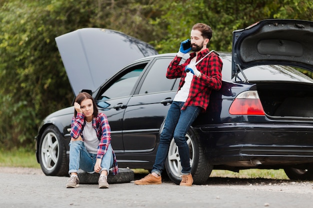 Woman sitting on tire and man talking on phone