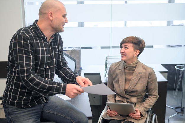 Free photo woman sitting in wheelchair taking to a coworker