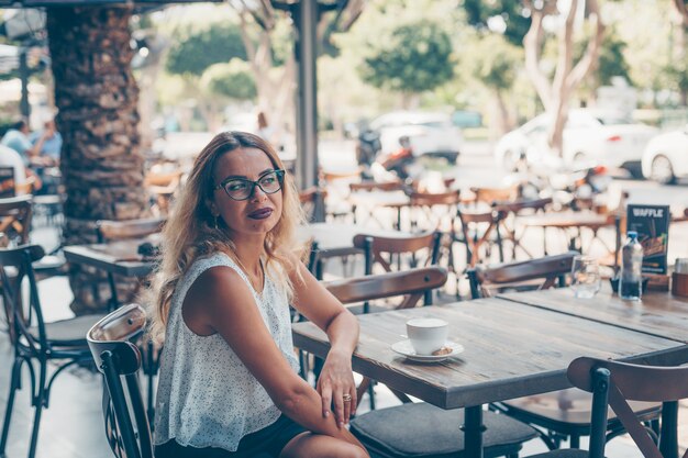 woman sitting and in white textured shirt at cafe terrace during daytime.