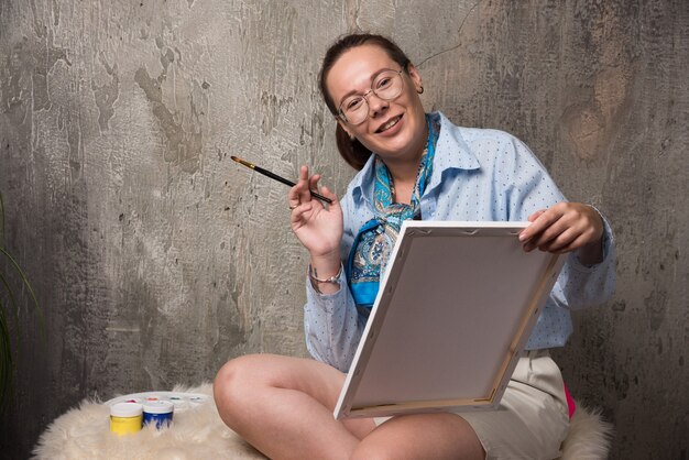 Woman sitting with canvas and brush on marble background . High quality photo