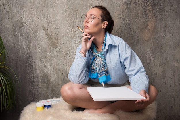 Woman sitting with canvas and brush on marble background . 