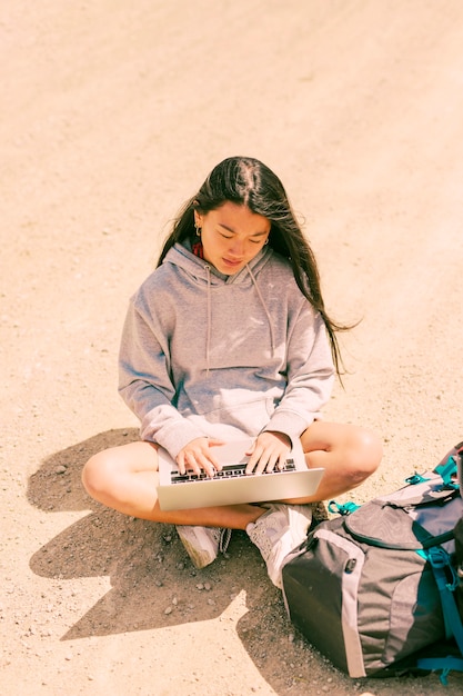 Woman sitting with crossed legs on road and working on laptop 