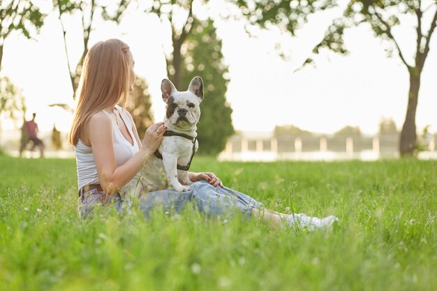 芝生の上にフレンチブルドッグと一緒に座っている女性