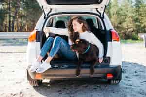 무료 사진 열린 트렁크에 그녀의 강아지와 함께 앉아있는 여자