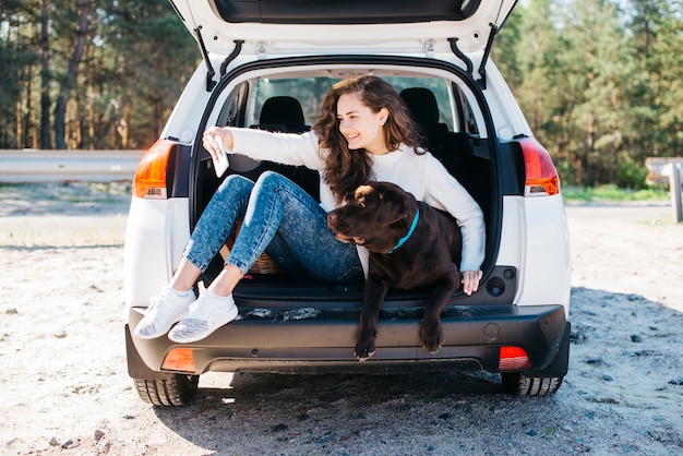 열린 트렁크에 그녀의 강아지와 함께 앉아있는 여자