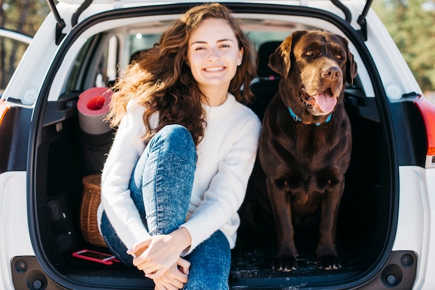 열린 트렁크에 그녀의 강아지와 함께 앉아있는 여자