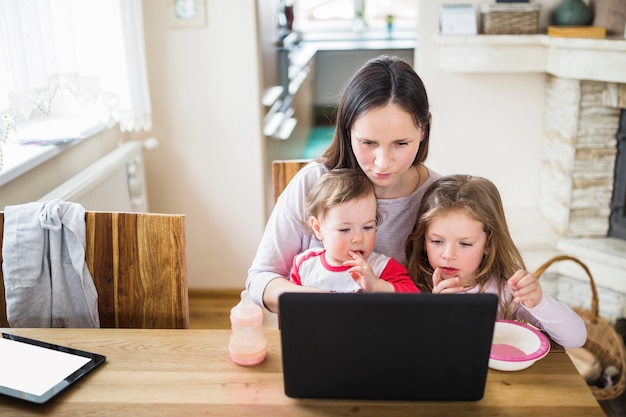 나무 책상 위에 노트북에서 일하는 그녀의 아이들과 함께 앉아있는 여자